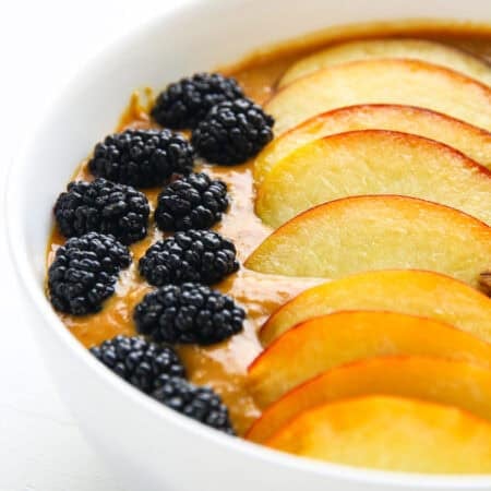 A thick apricot smoothie bowl topped with peach slices, blackberries, and granola.