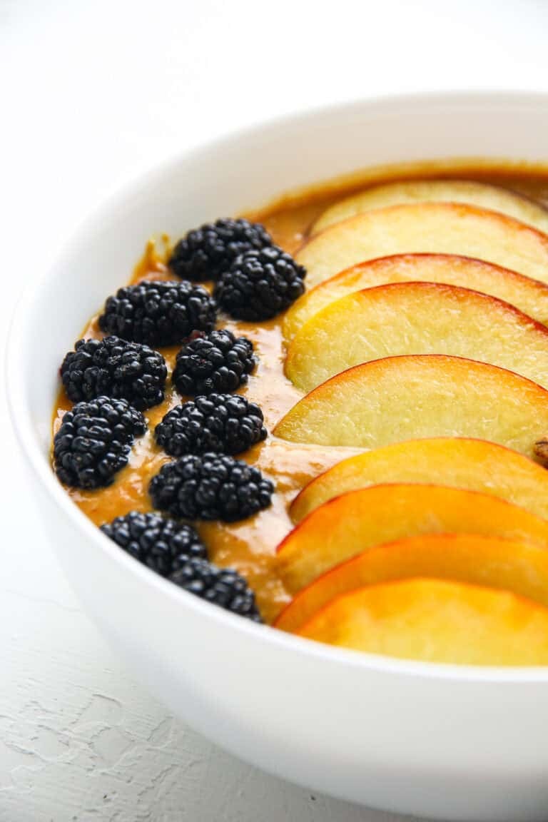 A thick apricot smoothie bowl topped with peach slices, blackberries, and granola.