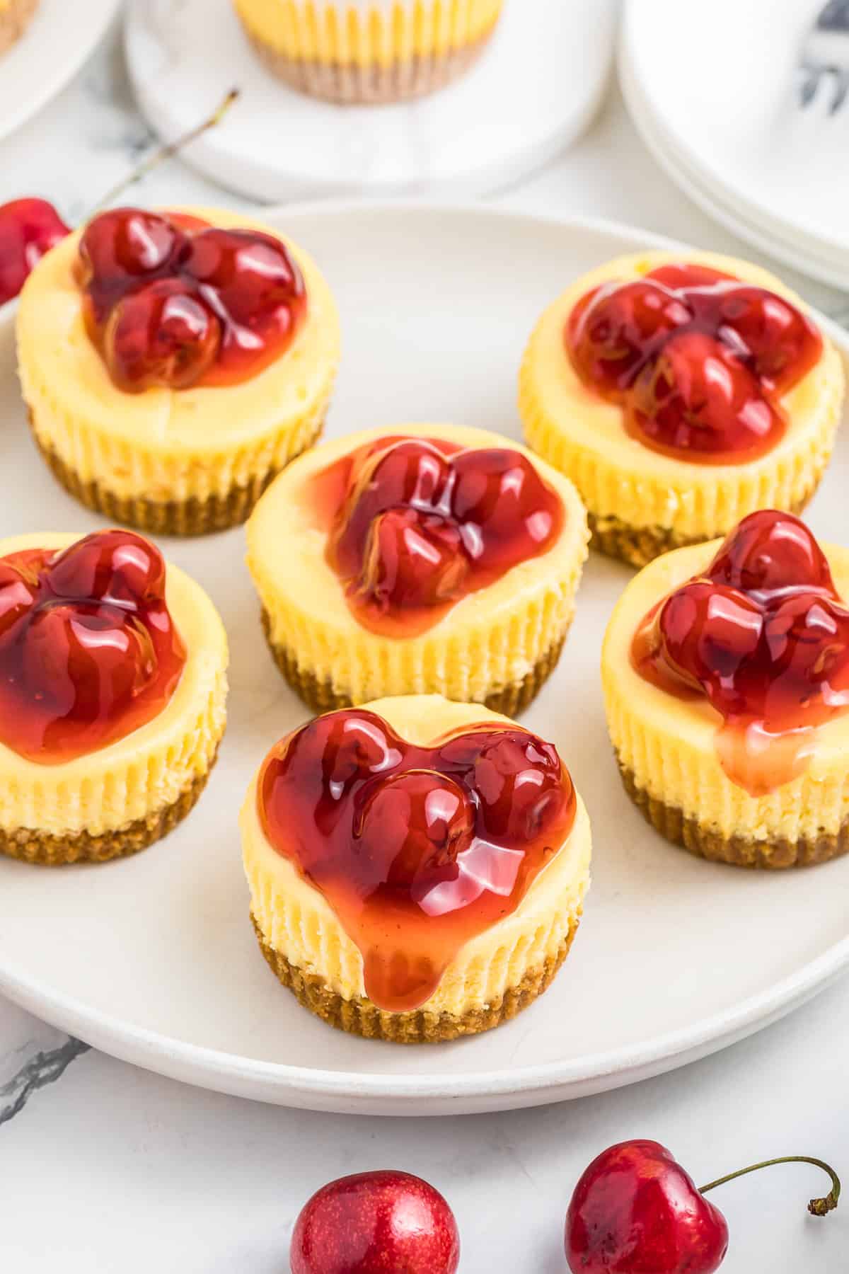 This picture is a overhead picture of 6 mini cheesecakes with the cherry sauce drizzled over the mini cheescakes.