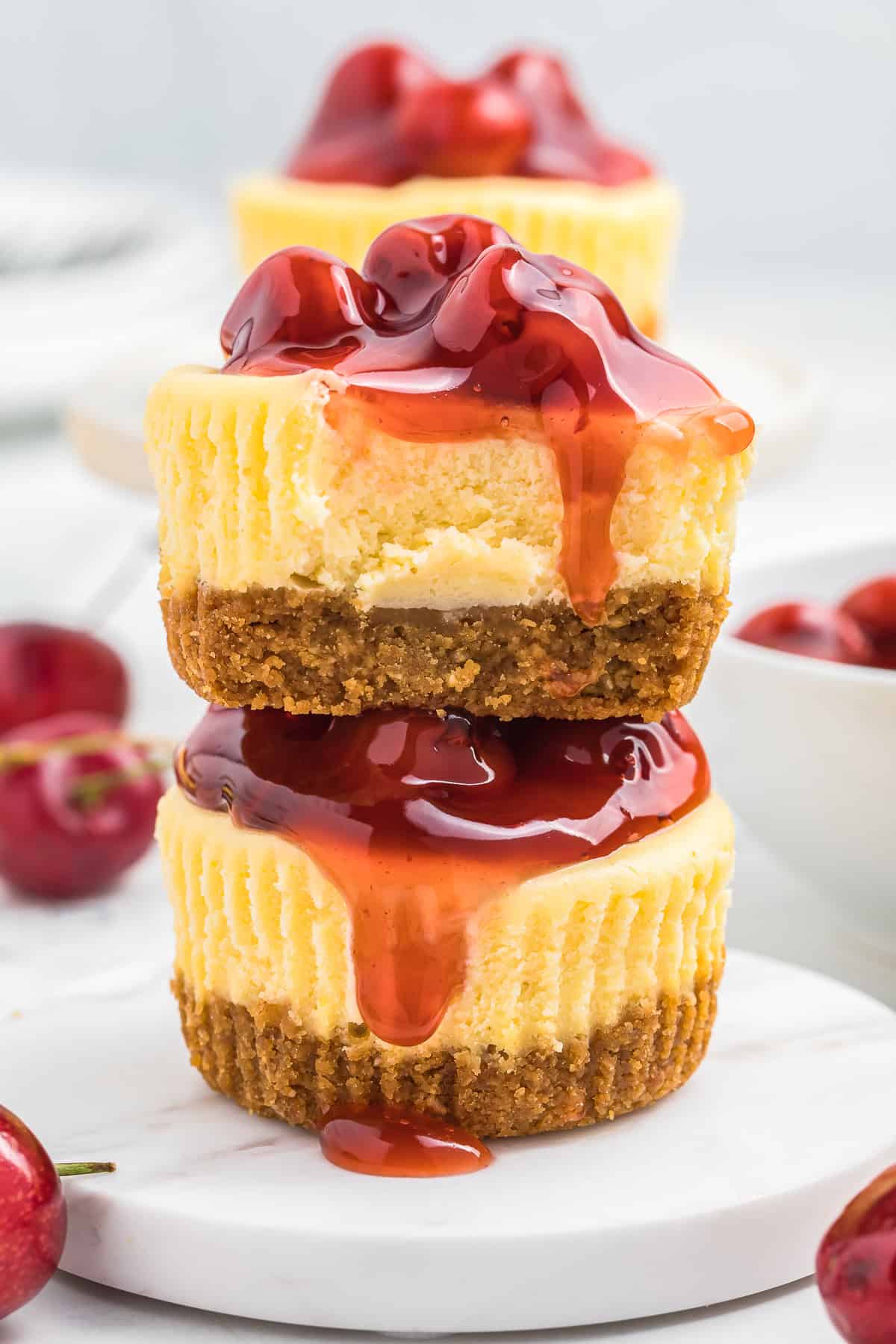 This is a picture of two mini cheesecakes stacked on top of each other. Both are dripping cherry juice off the side.