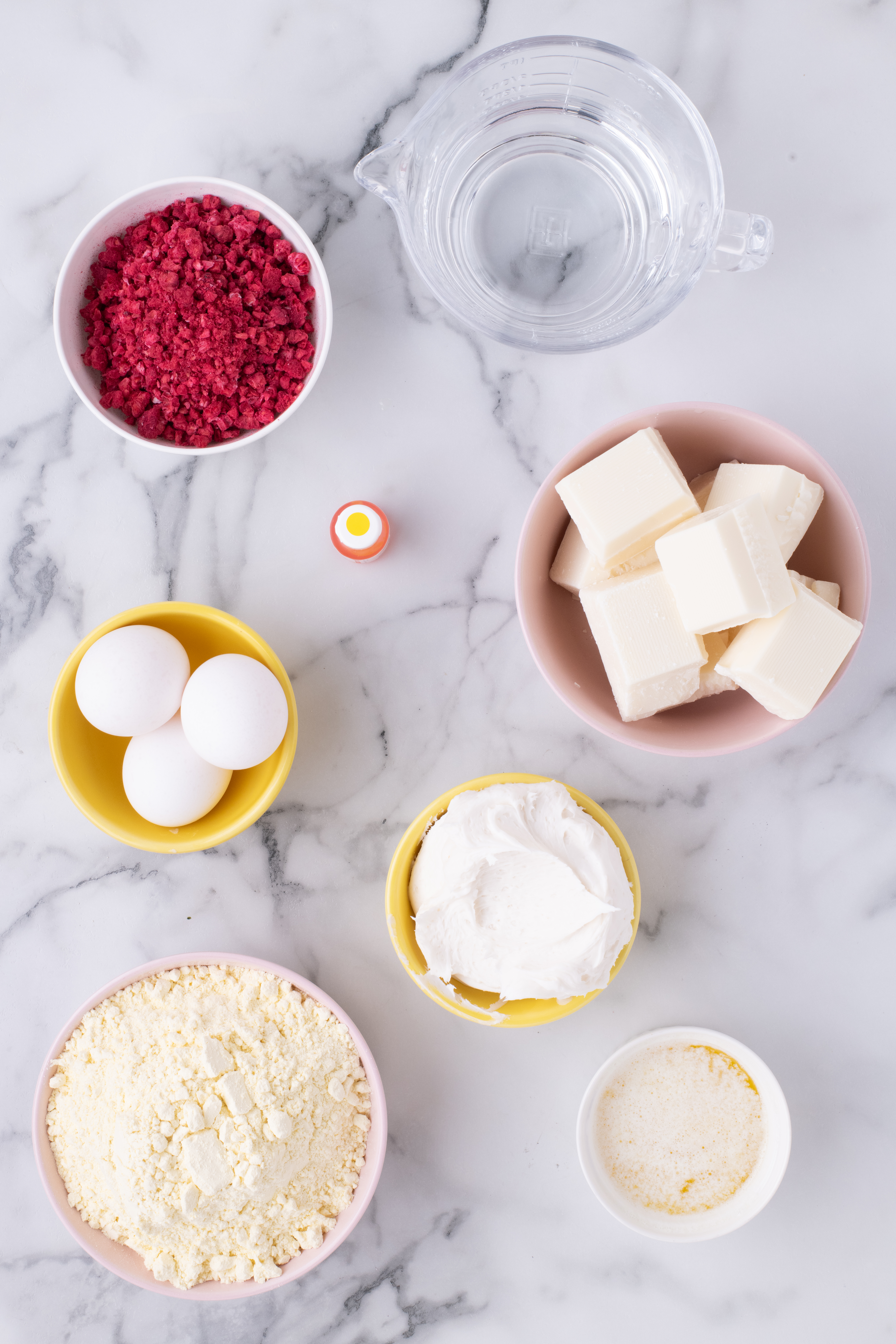 Ingredients for lemon raspberry cake balls including cake mix, eggs, water, frosting, white chocolate and freeze-dried raspberries.