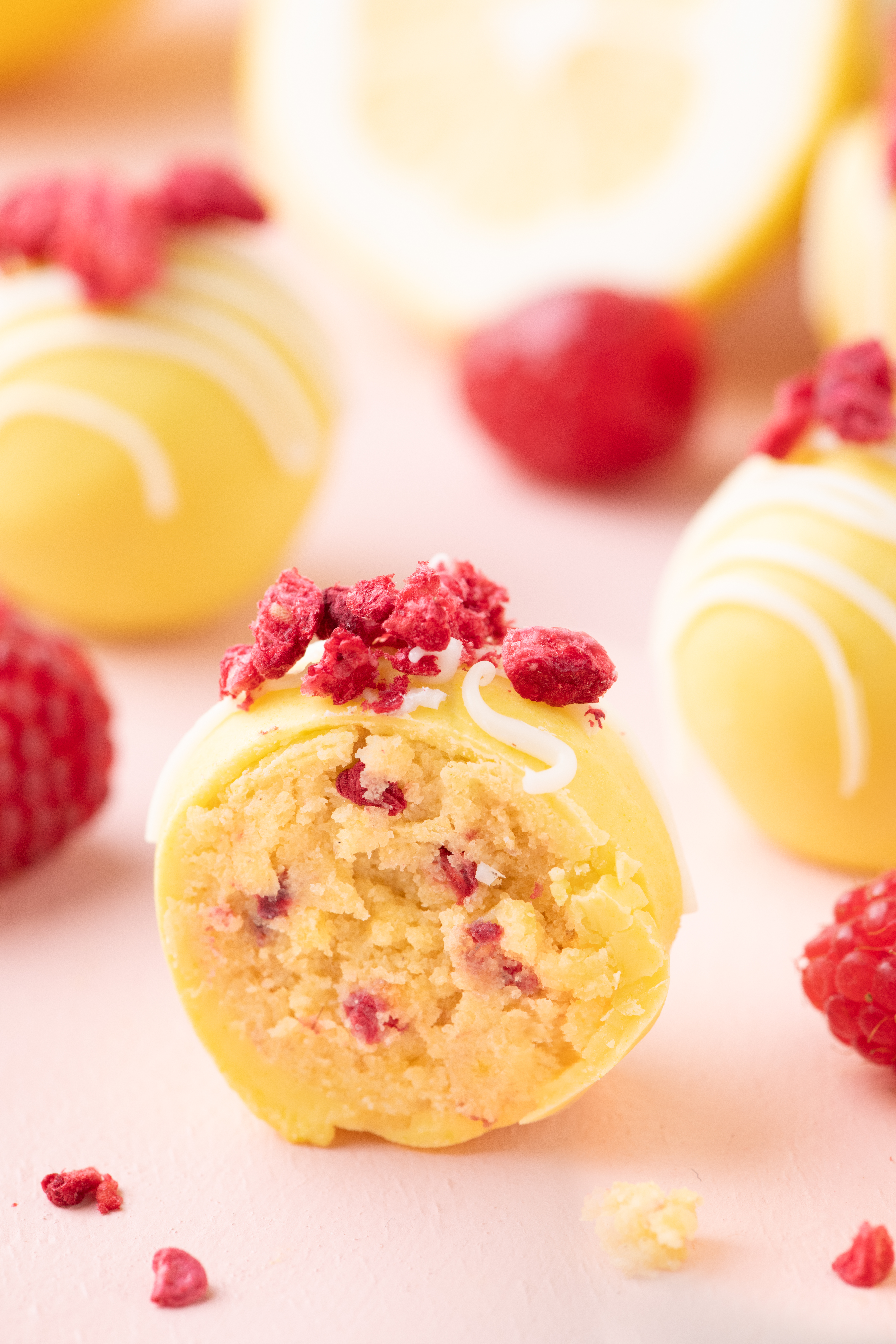 Close up lemon raspberry cake balls showing soft lemon cake interior with raspberry bits and white chocolate coating.