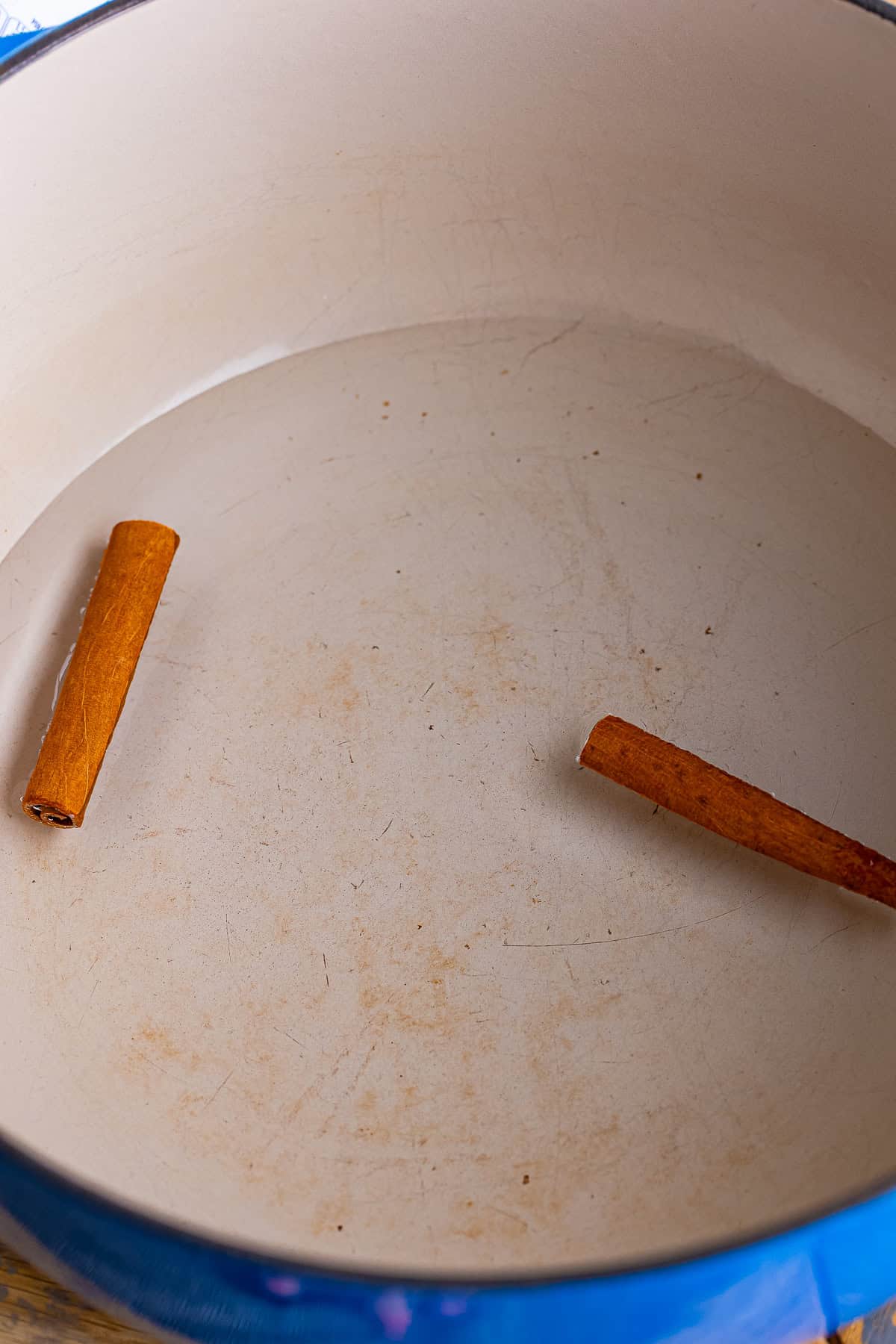 Two cinnamon sticks placed in a large white pot to start making Mexican Rice Pudding.