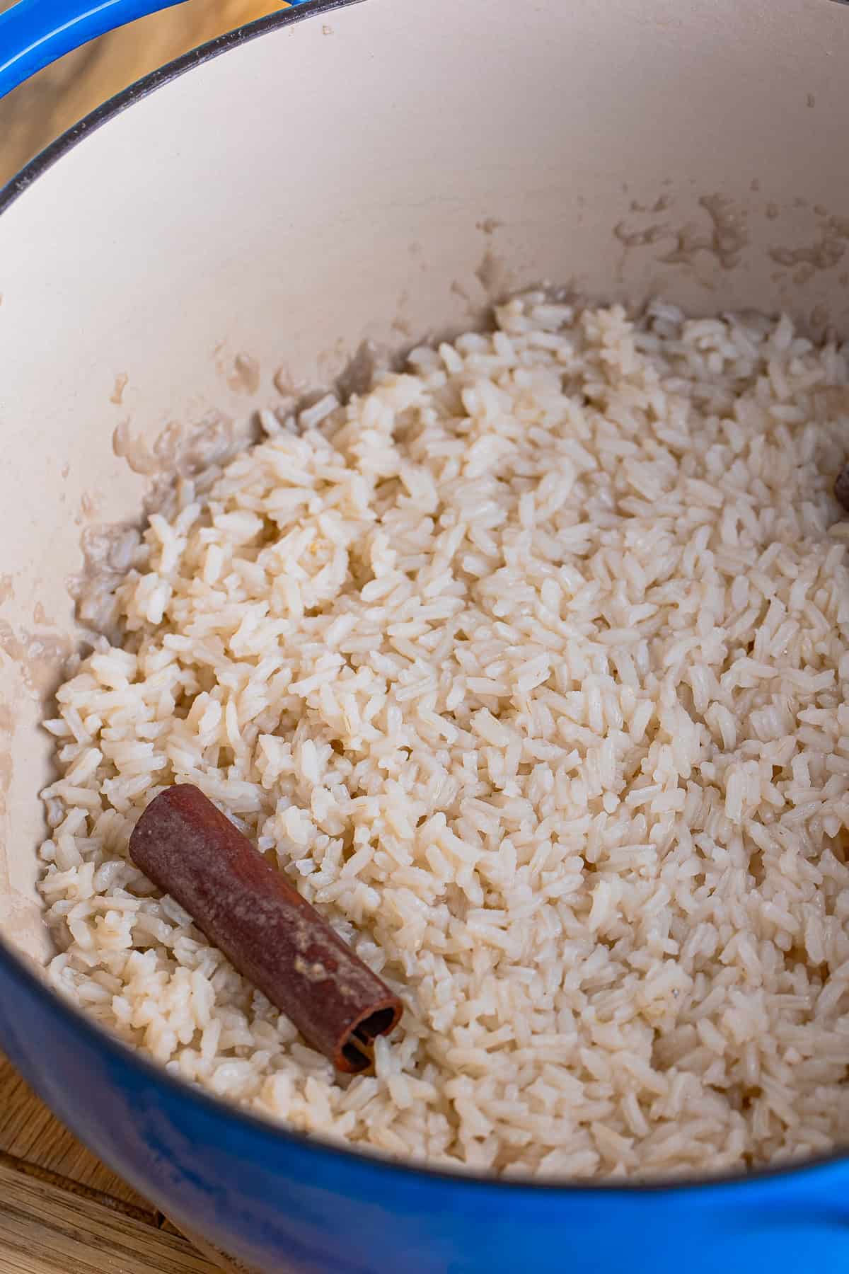 Cooked rice with a cinnamon stick in a large pot after simmering in cinnamon-infused water for Mexican Rice Pudding.