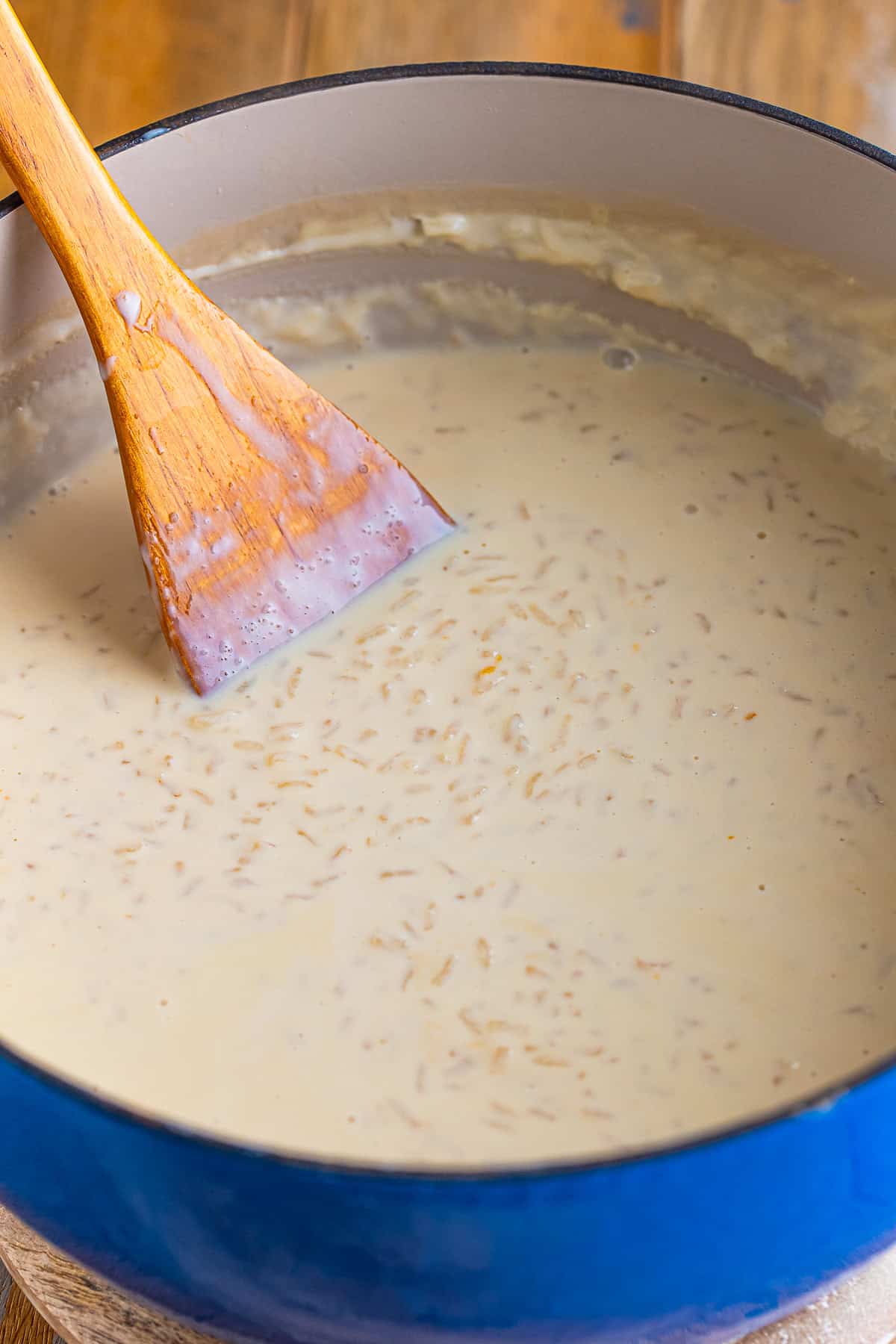Stirring the creamy rice and milk mixture in a large pot with a wooden spoon while making Mexican Rice Pudding.