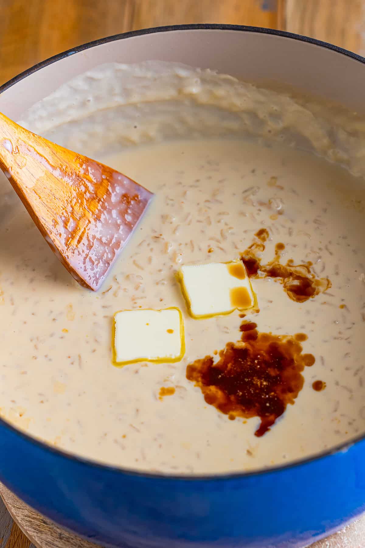 Butter pats and vanilla extract being added to the thick and creamy Mexican Rice Pudding in a pot.