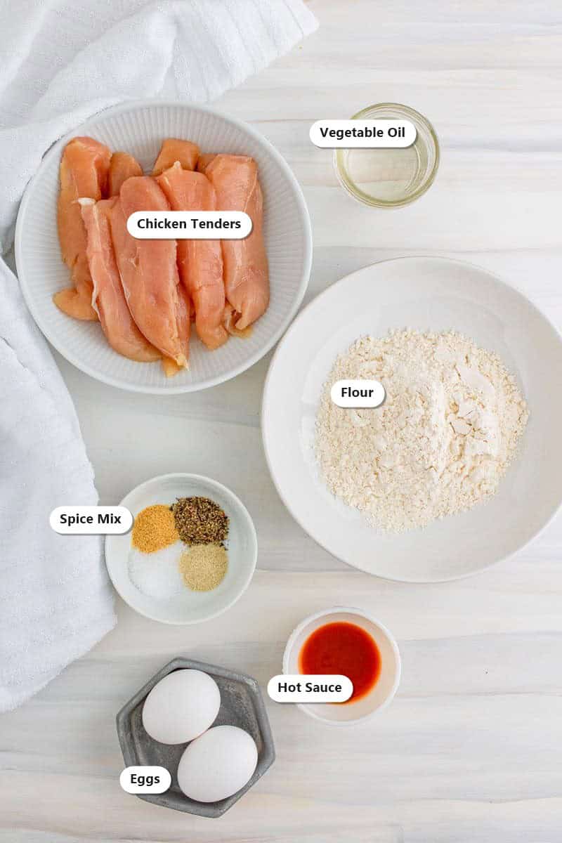 Labeled ingredients for Air Fryer Buffalo Chicken Tenders Recipe including chicken tenders, flour, eggs, hot sauce, salt, and spices.