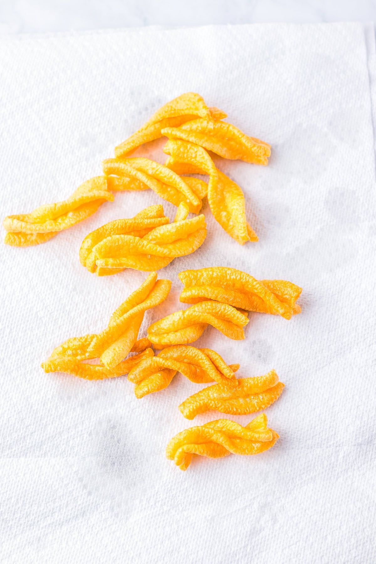 Puffed duros being lifted out of the hot oil with a slotted spoon onto a paper towel lined tray for the Copycat Taco Bell Cinnamon Twists Recipe.