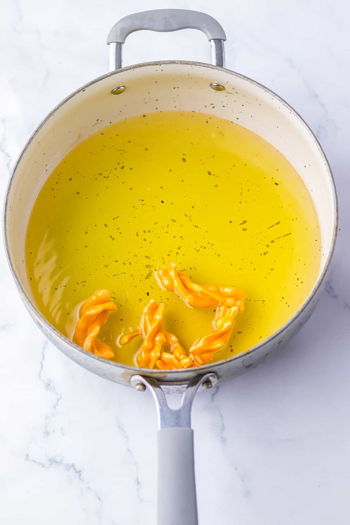 Vegetable oil heating in a high-sided skillet to 350 degrees with a few spiral duros being added to puff up for the Copycat Taco Bell Cinnamon Twists Recipe.