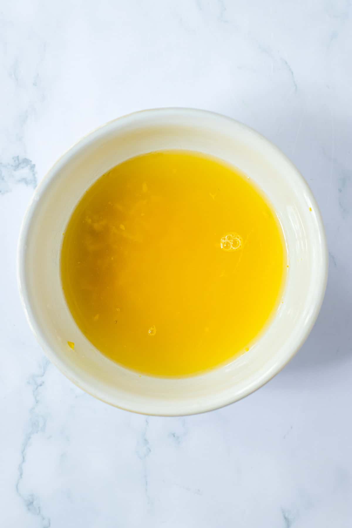 A small bowl with chicken broth, fresh lemon juice, and lemon zest stirred together for slow cooker lemon chicken thighs.