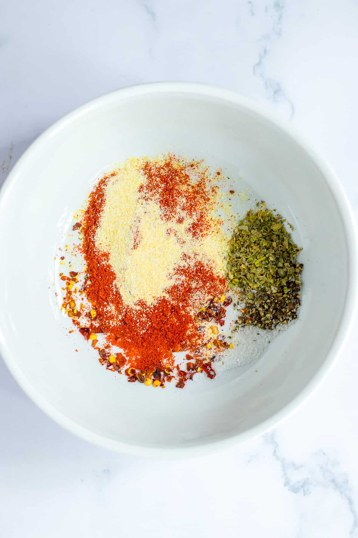 A small bowl of Italian seasoning, onion powder, garlic powder, paprika, red pepper flakes, salt, and black pepper mixed for slow cooker lemon chicken thighs.