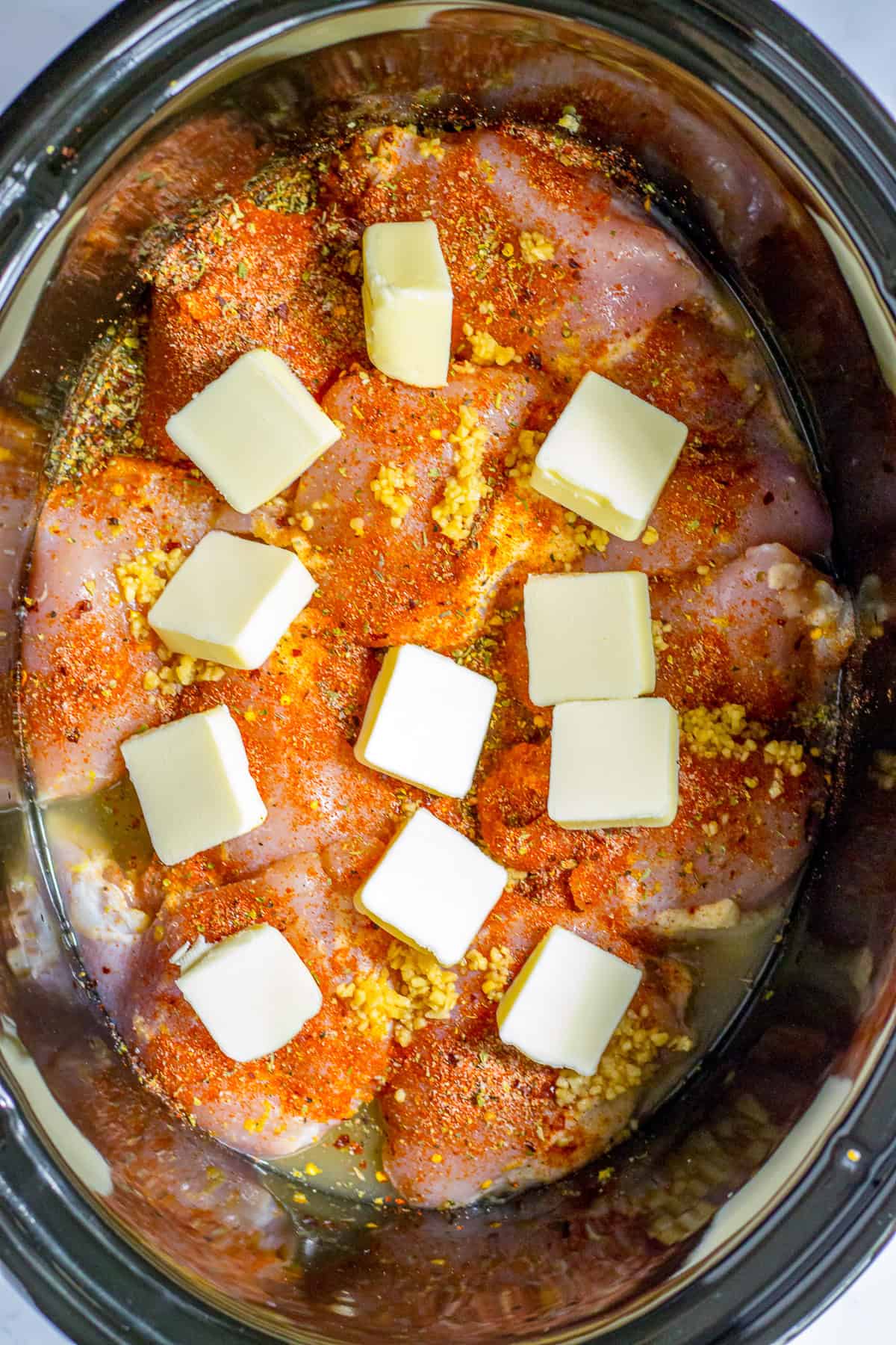 Boneless skinless chicken thighs in a slow cooker with dry seasoning, minced garlic, and butter slices on top for slow cooker lemon chicken thighs.