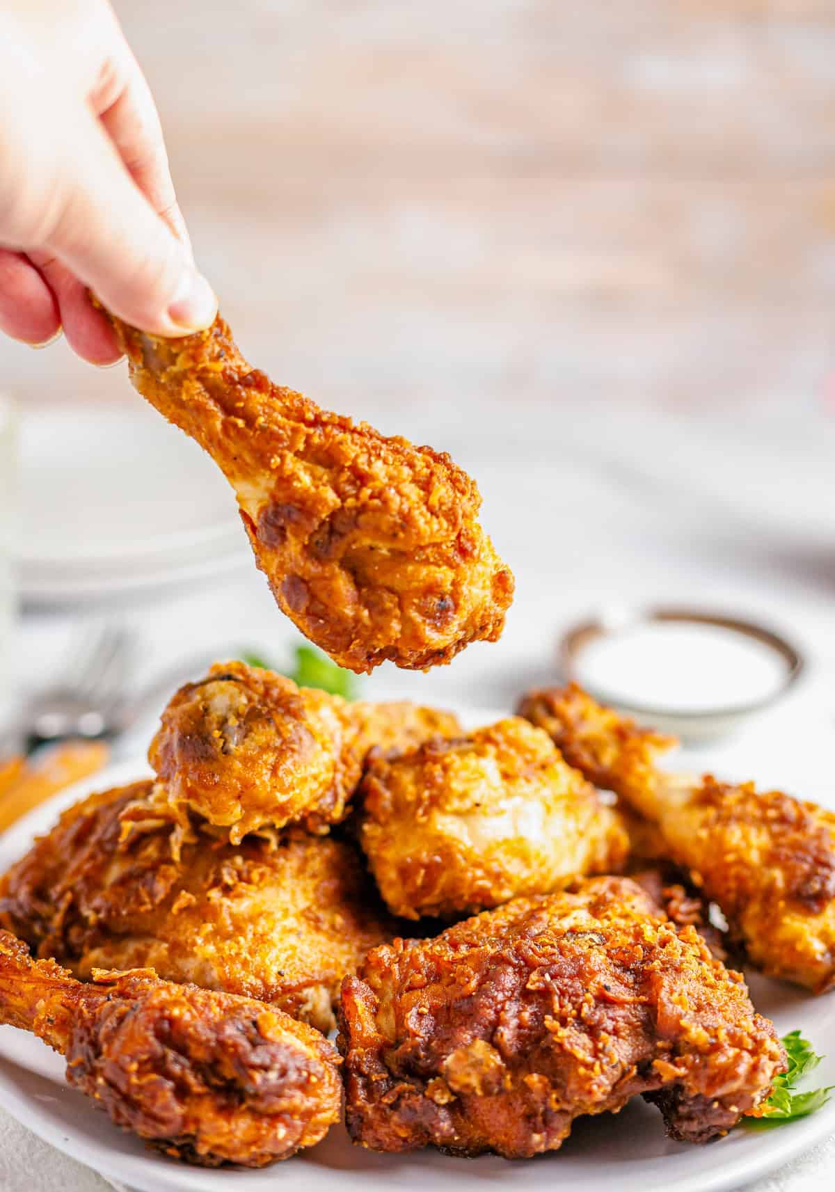 Hand grabbing a piece of Crispy Southern Fried Chicken from a platter with the crunchy crust pulling away.