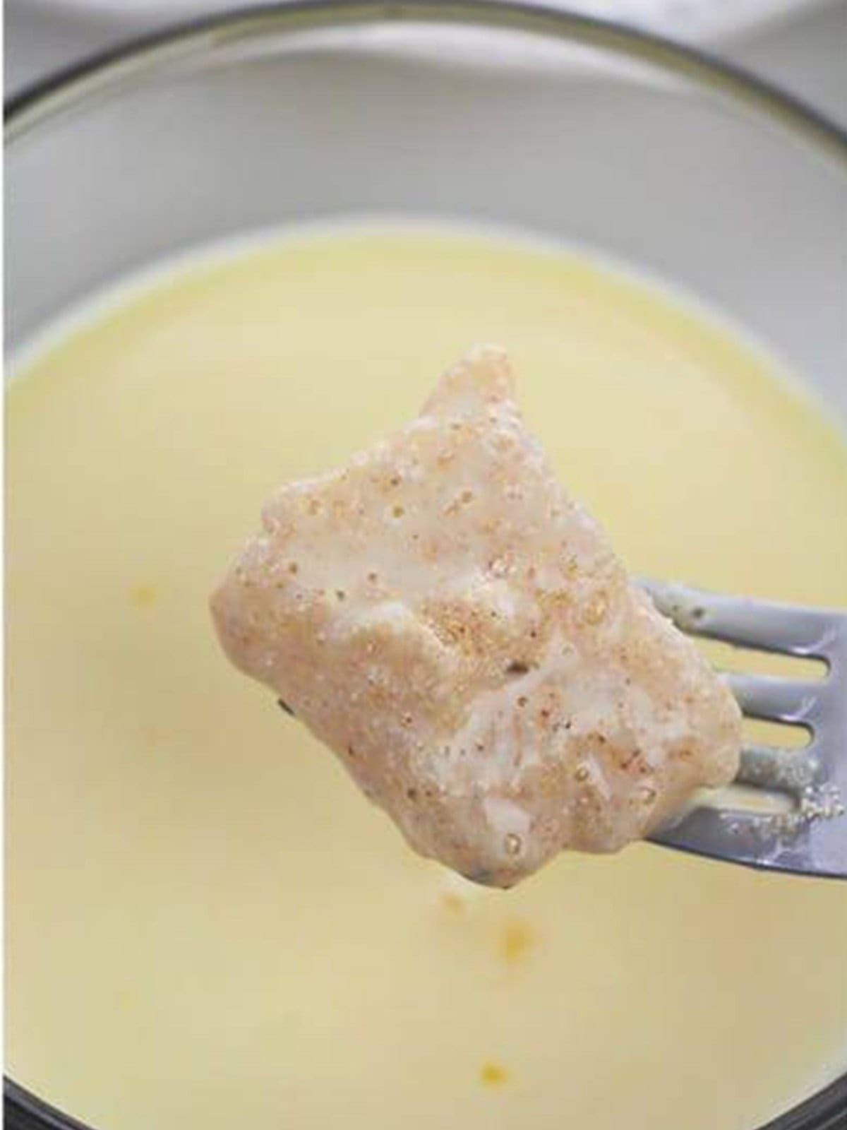 Catfish nugget dipped in the buttermilk and egg mixture on a fork.