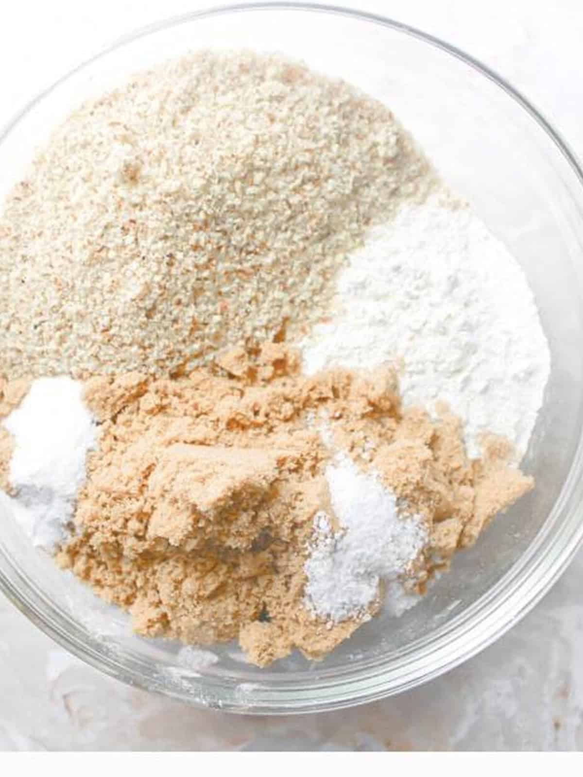 Flour, ground almonds, brown sugar, baking soda, and salt combined in a glass bowl for almond cookies.