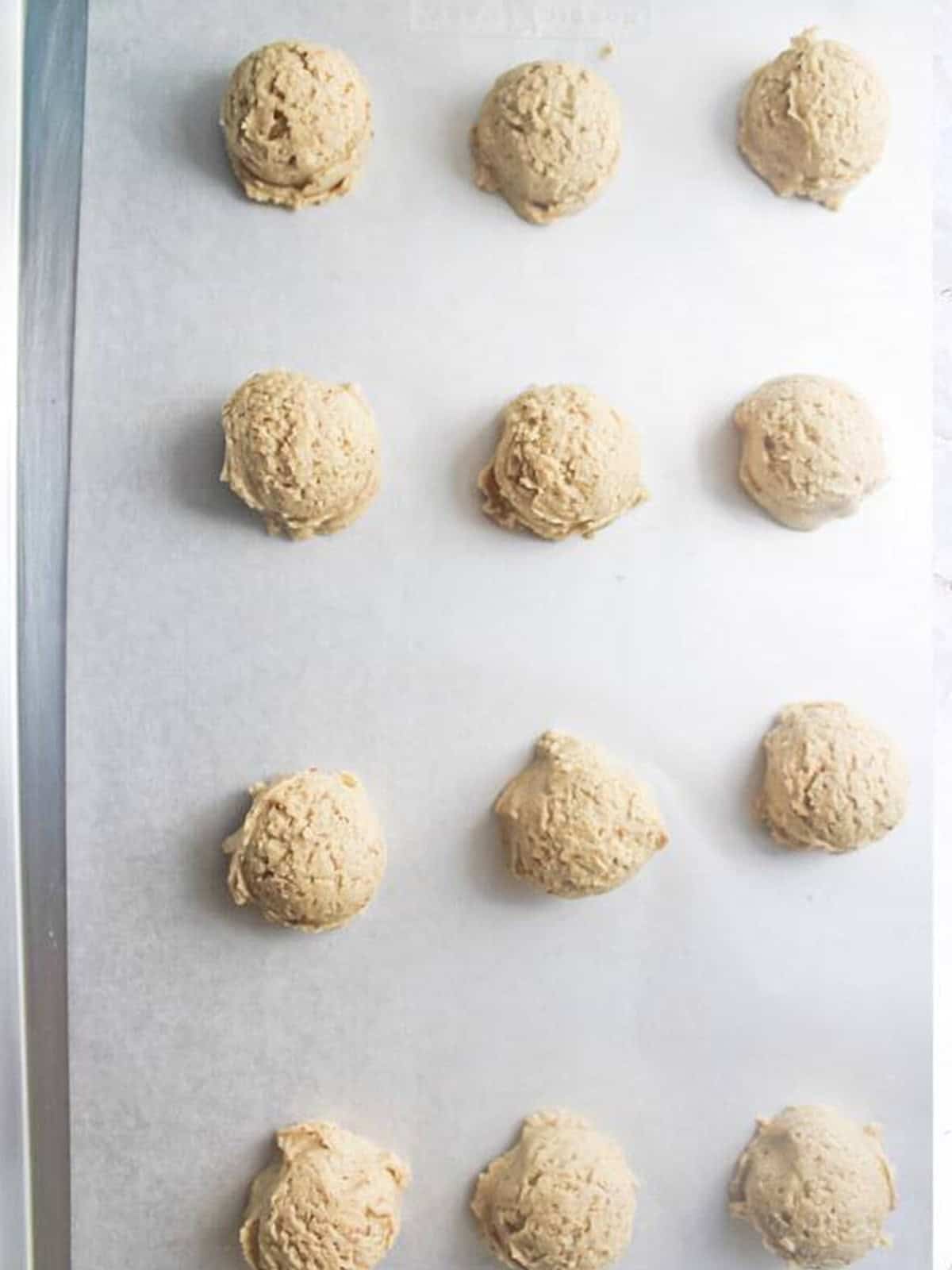 Scoops of almond cookie dough portioned onto a parchment lined baking sheet.