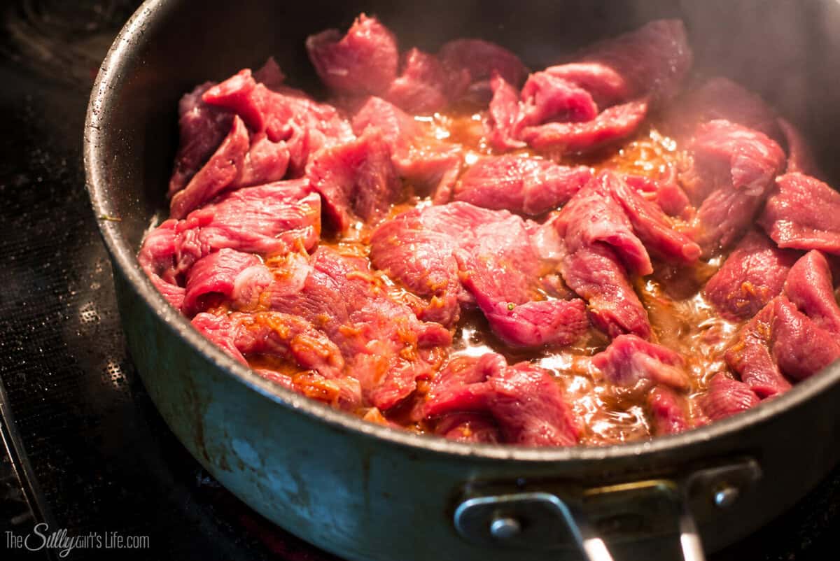 Marinated flank steak strips searing in a hot cast iron skillet after the Beef and Broccoli Marinade has worked its magic.