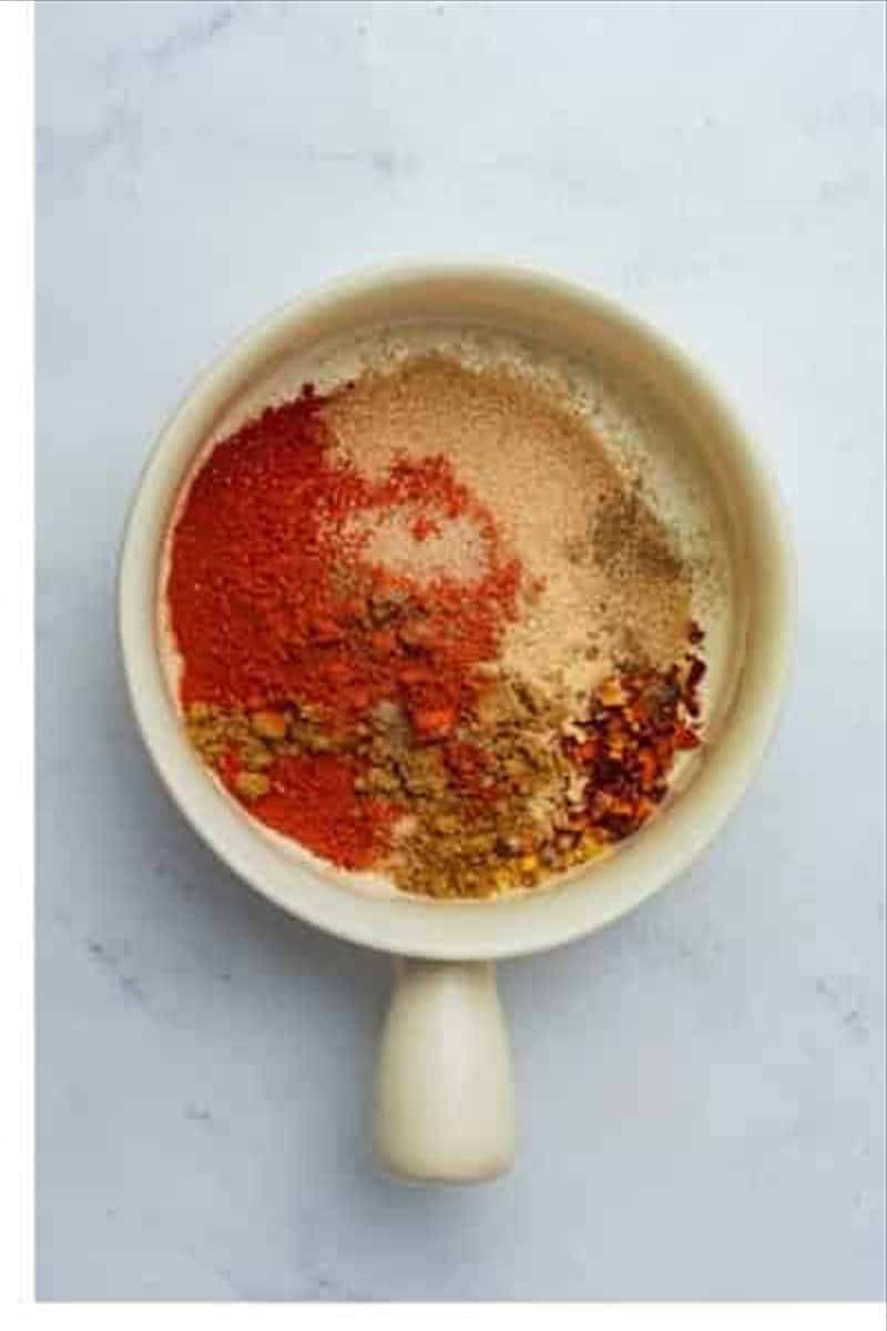 Small ceramic bowl filled with brown sugar, paprika, cumin, garlic powder, onion powder, chili powder, salt, and pepper for Best Oven St Louis Ribs Recipe.
