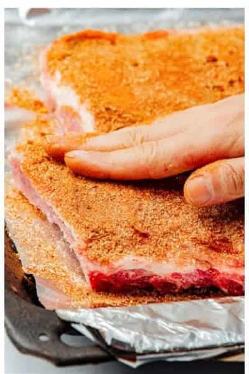 Hand rubbing dry spice rub onto a rack of St Louis Ribs on foil-lined baking tray for Best Oven St Louis Ribs Recipe.