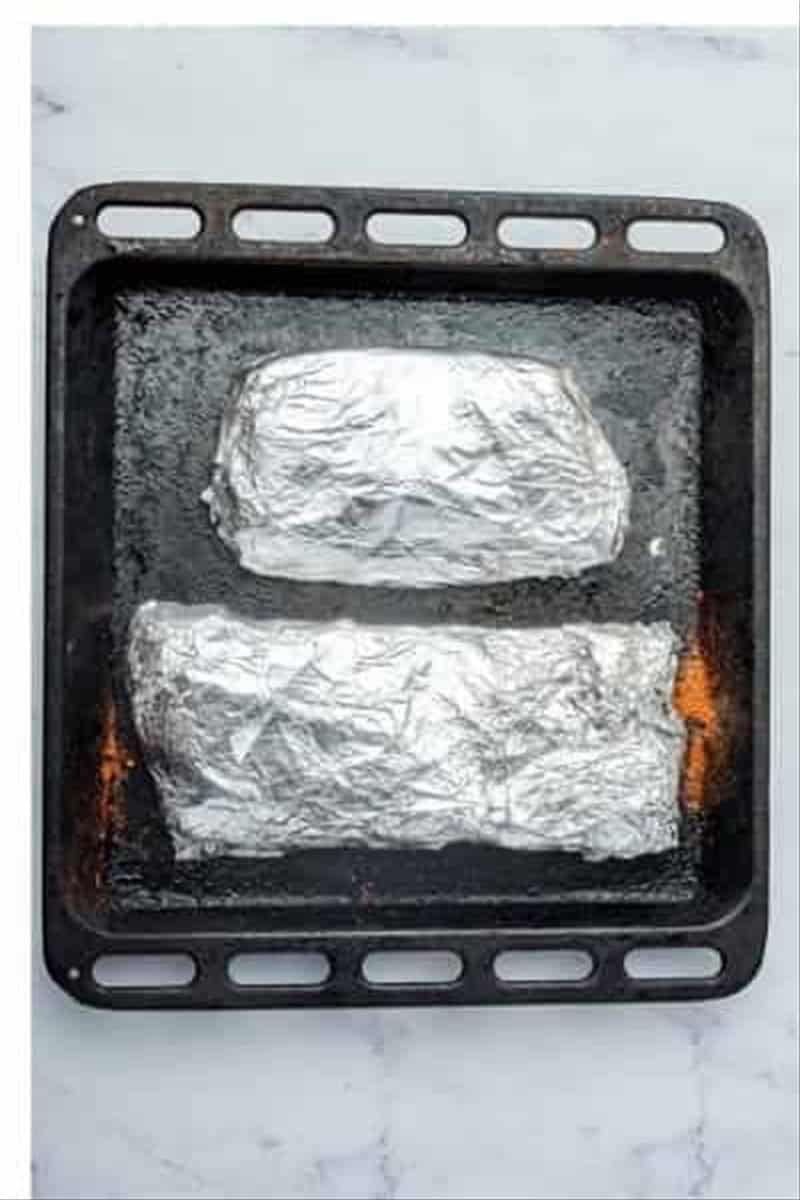 Two foil-wrapped racks of St Louis Ribs on a dark baking tray ready for the oven for Best Oven St Louis Ribs Recipe.