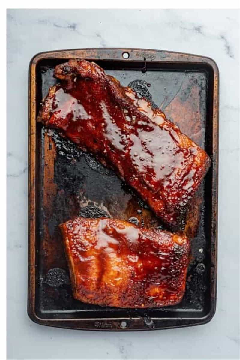 Two finished glazed racks of Best Oven St Louis Ribs resting on a dark baking tray after final glaze and bake.