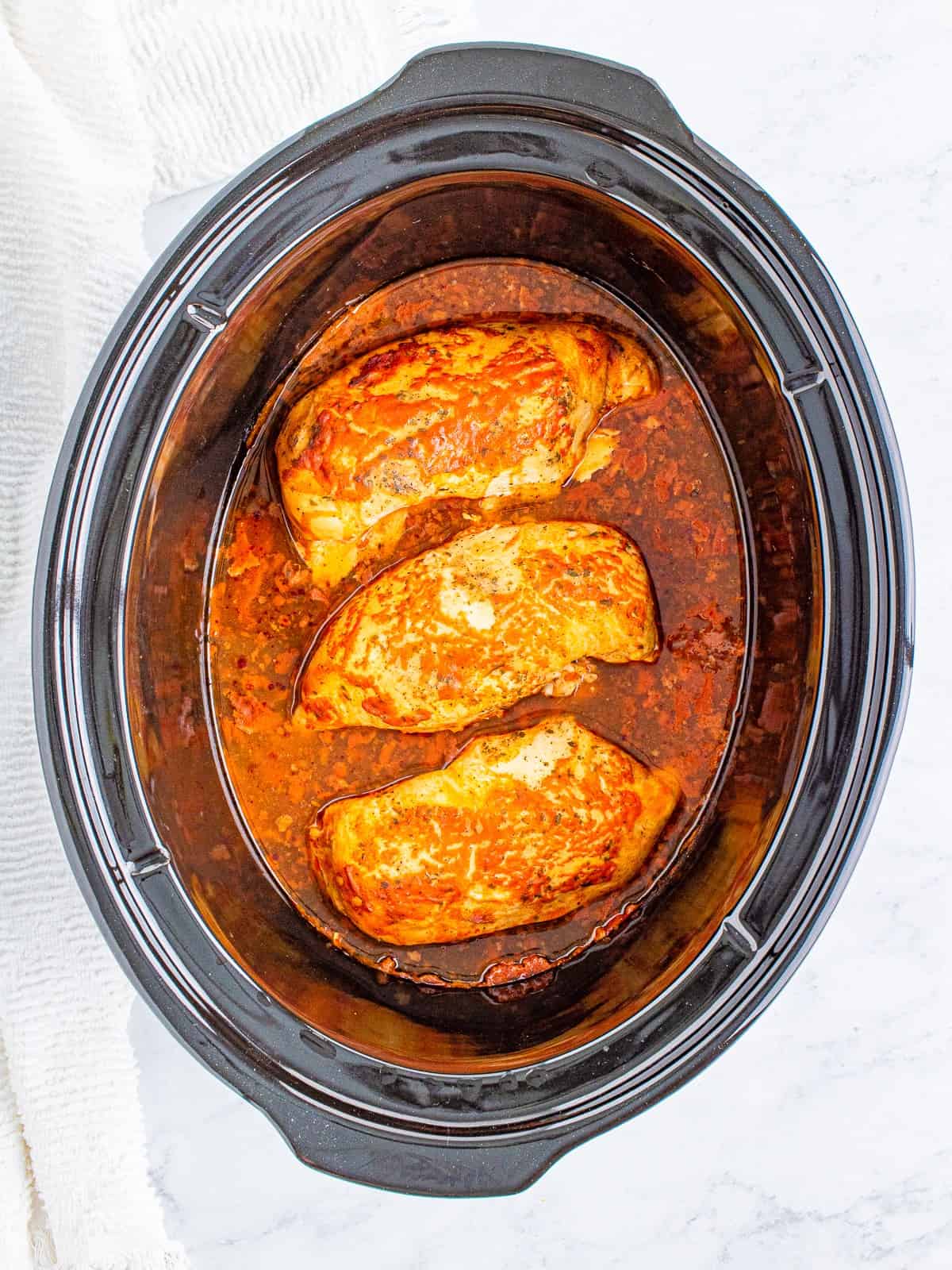 Cooked chicken breasts in buffalo sauce in the slow cooker.