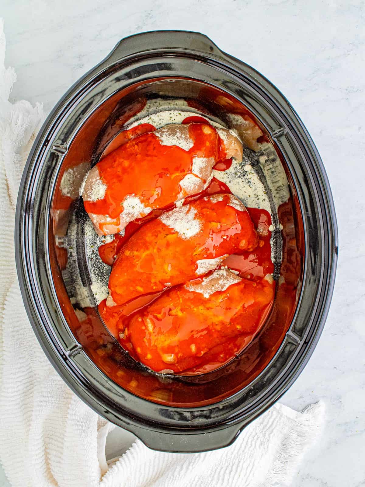 Chicken breasts with ranch seasoning and buffalo sauce in a slow cooker for buffalo chicken sandwiches.