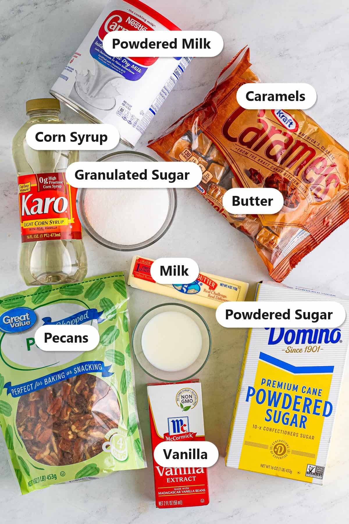 Labeled ingredients for caramel pecan logs including corn syrup, powdered milk, caramels, pecans, granulated sugar, milk, butter, vanilla, and powdered sugar.