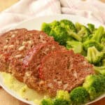 Sliced cheesy meatloaf served with steamed broccoli on a white plate.