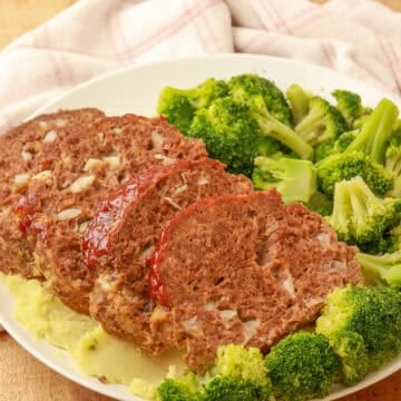 Sliced cheesy meatloaf served with steamed broccoli on a white plate.