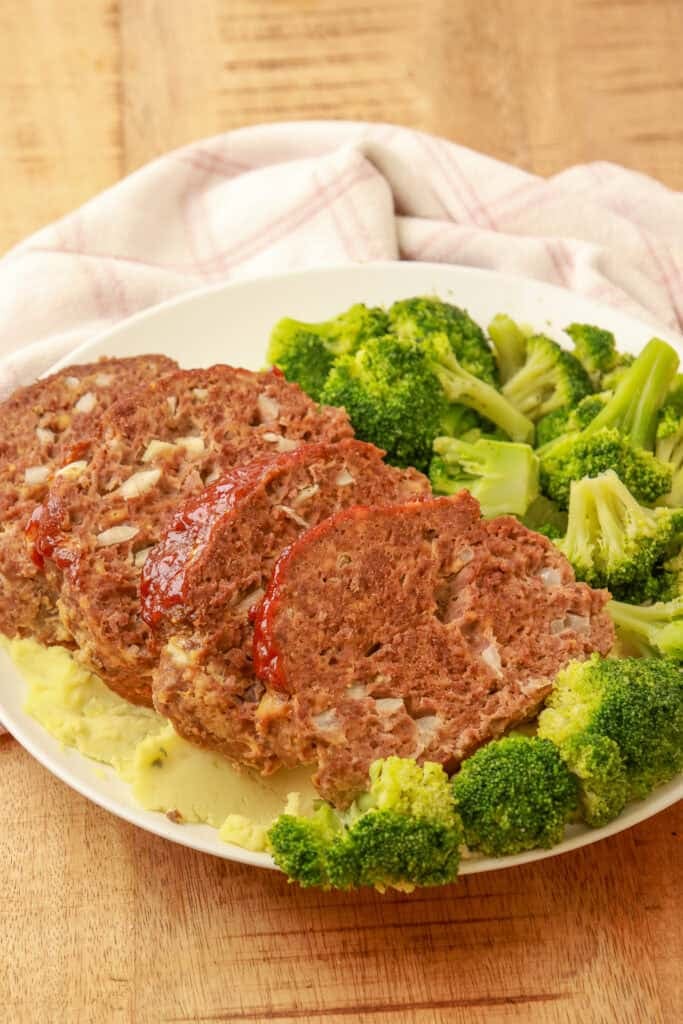 Sliced cheesy meatloaf served with steamed broccoli on a white plate.