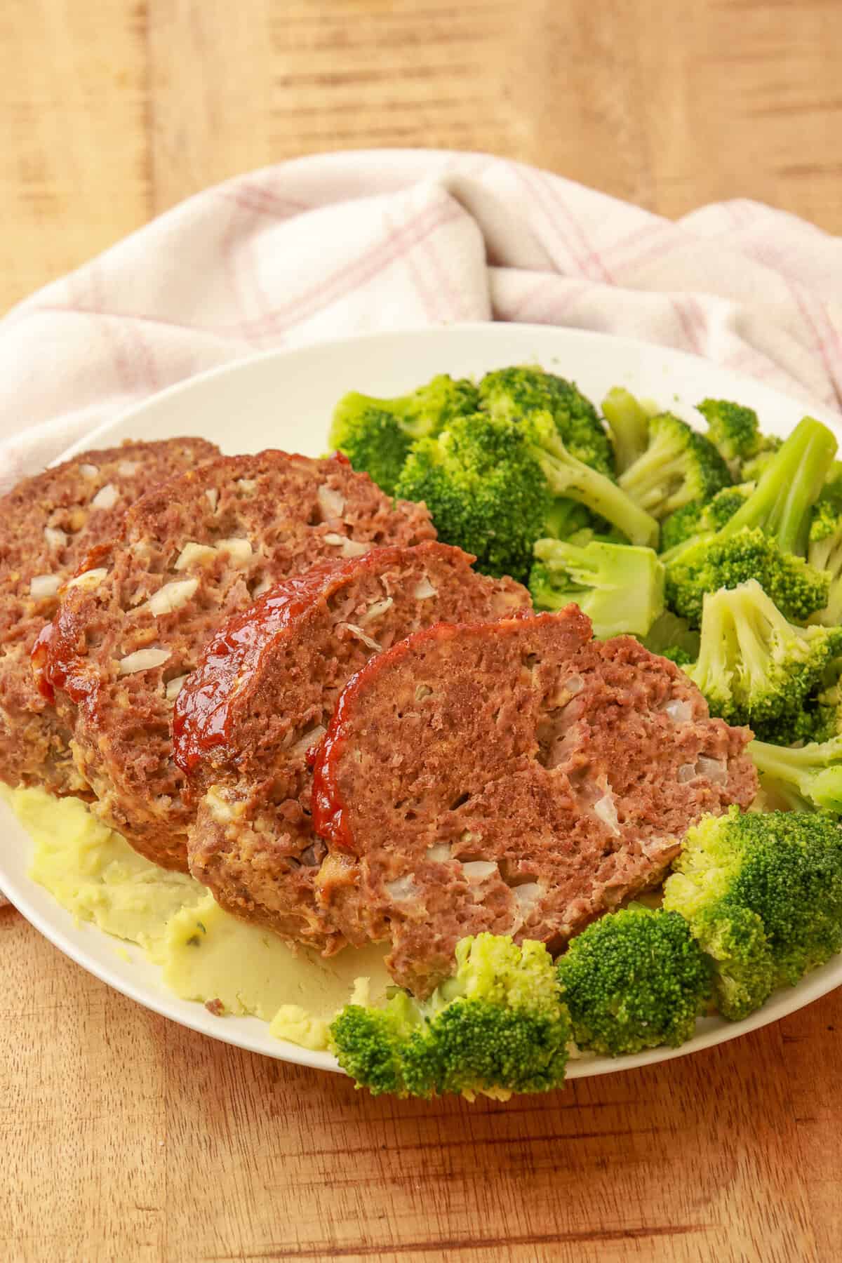 Sliced cheesy meatloaf served with steamed broccoli on a white plate.