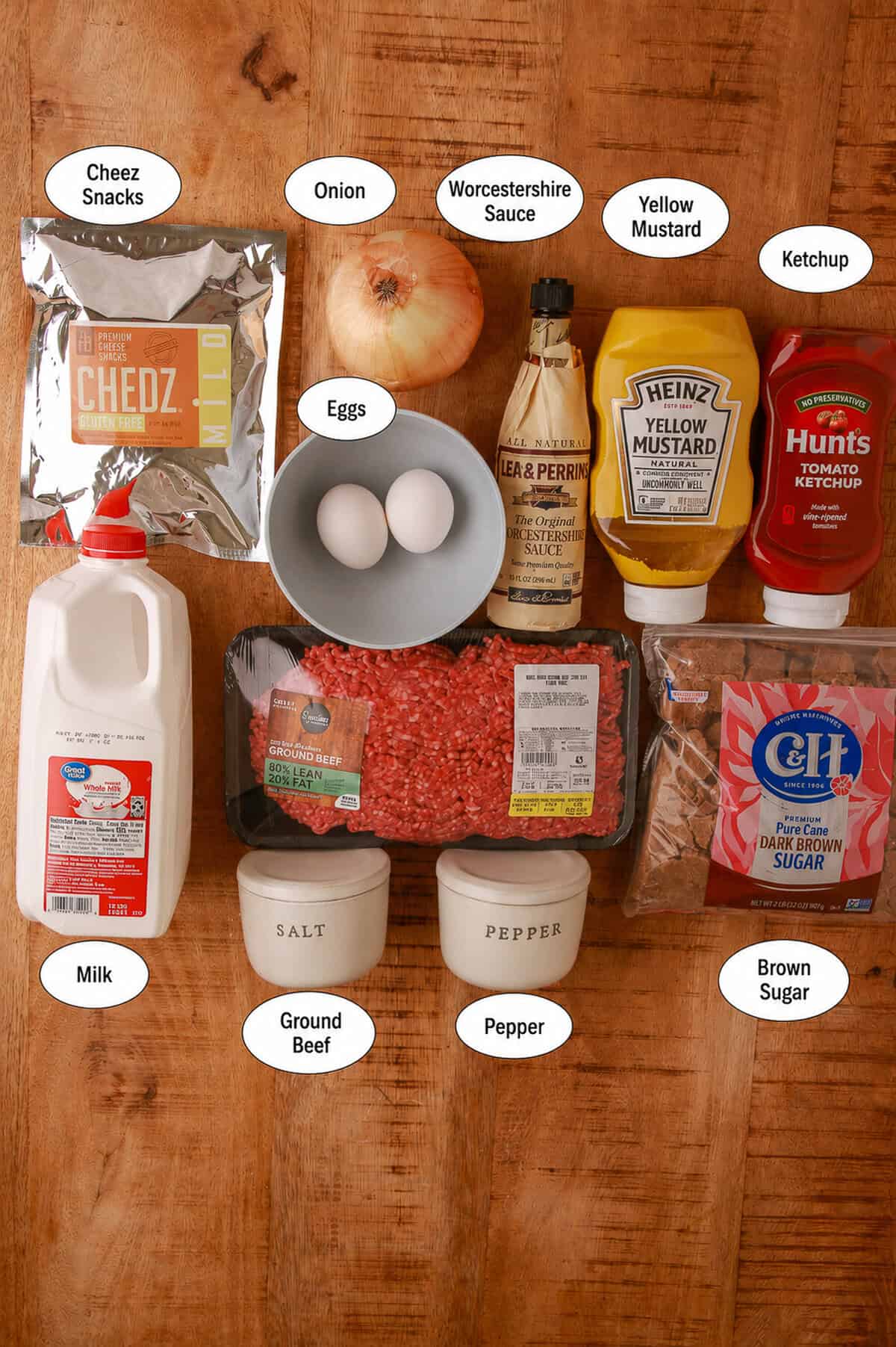 Labeled ingredients for cheesy meatloaf including Chedz snacks, ground beef, eggs, milk, onion, Worcestershire, yellow mustard, ketchup, brown sugar, salt, and pepper.