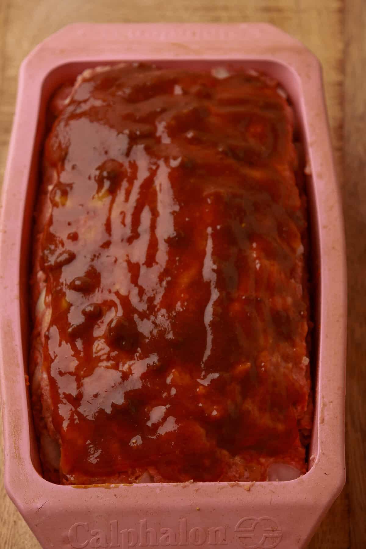 Cheesy meatloaf topped with brown sugar ketchup sauce ready to bake.
