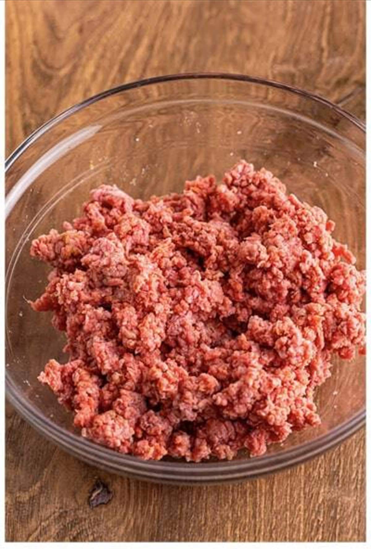 Seasoned ground beef mixed together in a glass bowl for cheeseburger sliders.