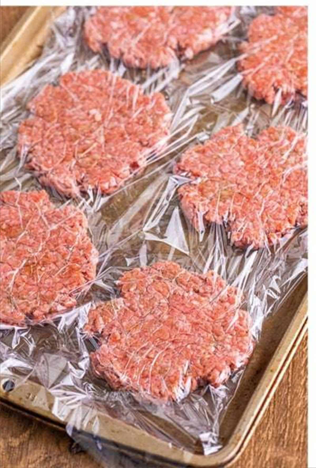 Ground beef balls pressed into flat patties on a sheet pan for cheeseburger sliders.