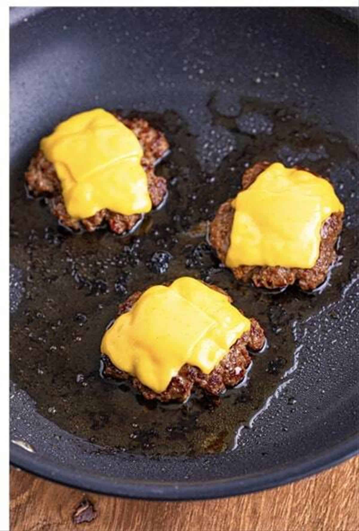 Cheeseburger slider patties topped with melted American cheese in a skillet.