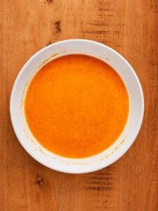 Eggs, water, and buffalo sauce whisked together in a glass bowl for the chicken wash.