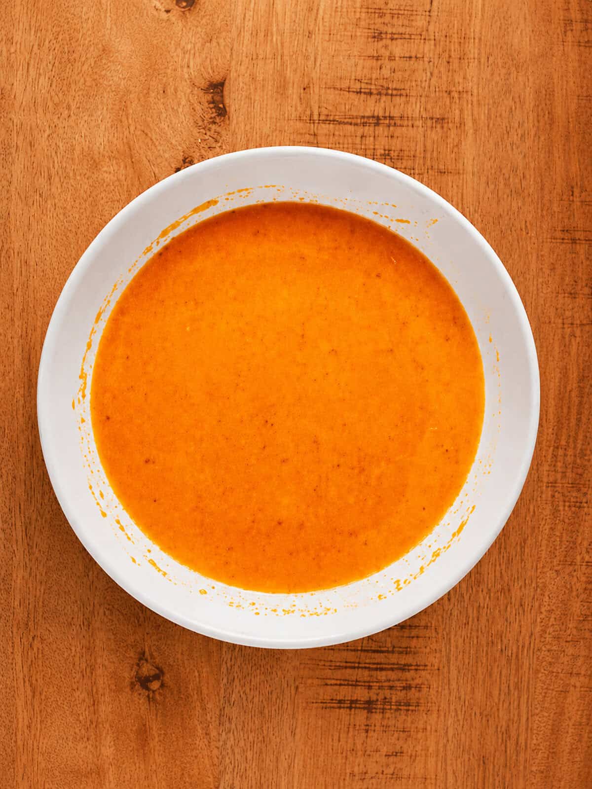Eggs, water, and buffalo sauce whisked together in a glass bowl for the chicken wash.