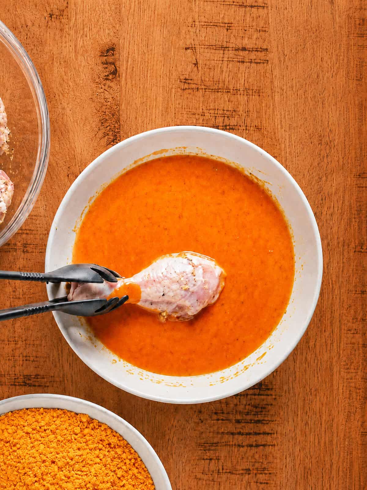 Chicken piece being dipped into the buffalo egg wash for cheesy fried chicken.