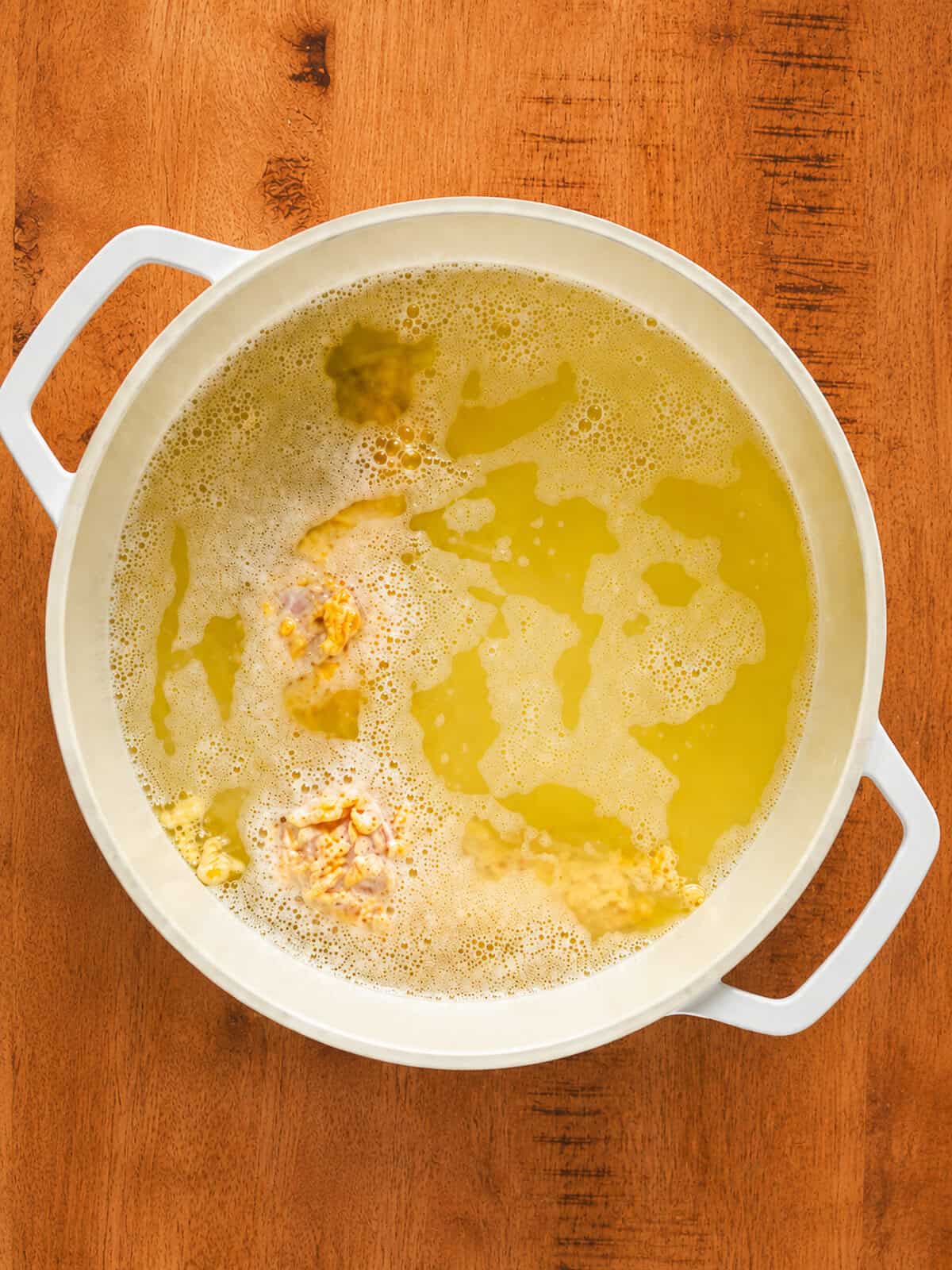 Cheesy fried chicken pieces frying golden brown in hot oil in a deep fryer.