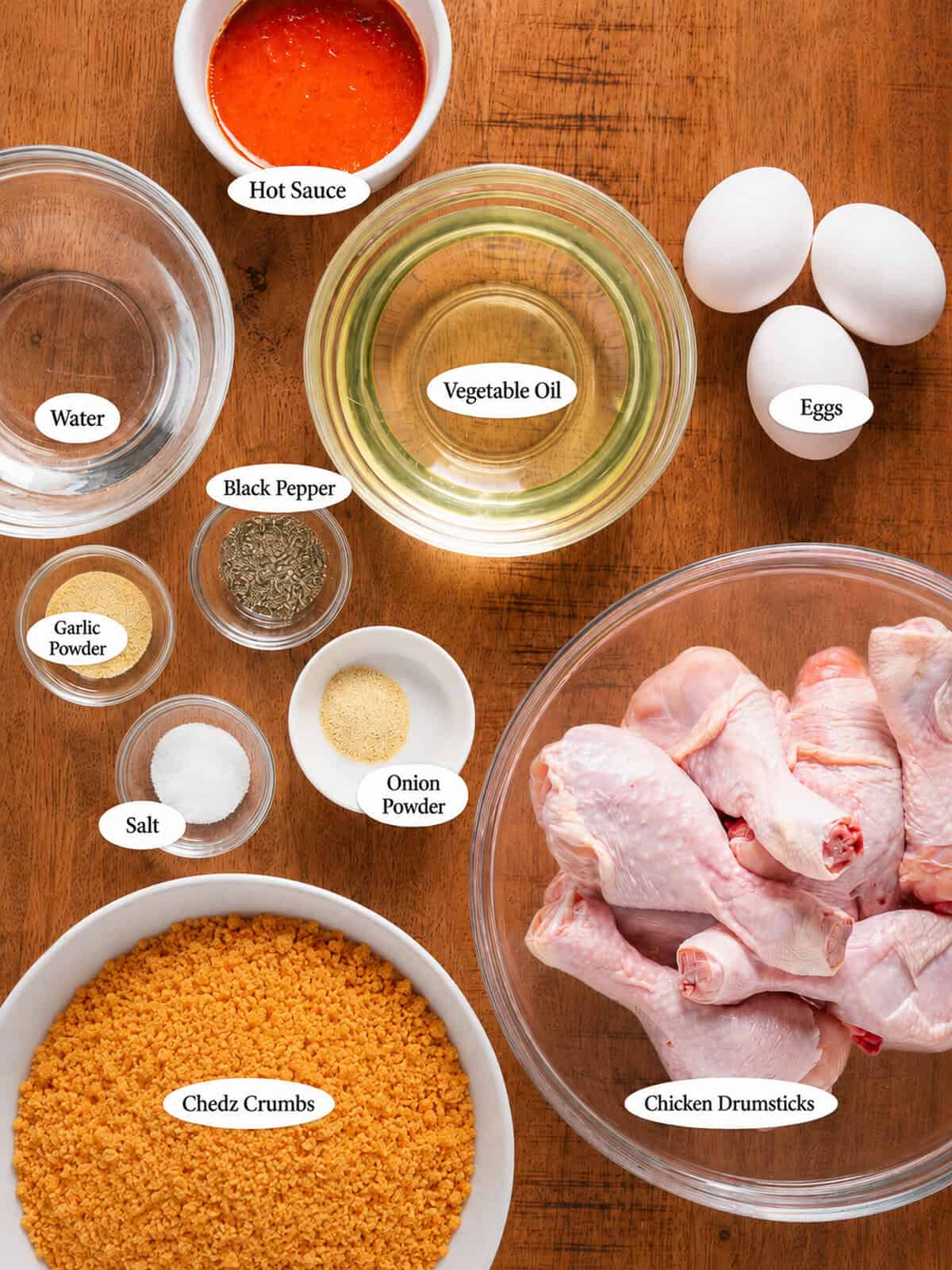 Labeled ingredients for cheesy fried chicken including Chedz crumbs, whole chicken, eggs, buffalo sauce, salt, pepper, garlic powder, and onion powder.