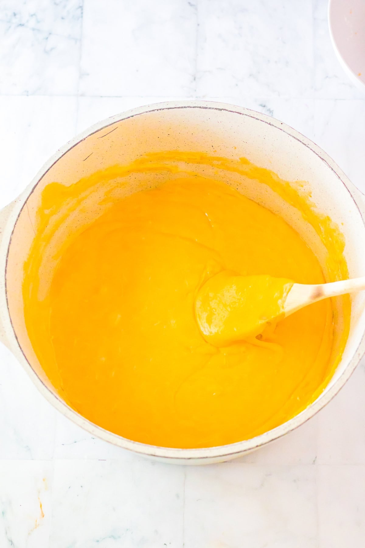 Smooth melted orange cheese sauce in a Dutch oven being stirred with a wooden spoon for Chick Fil A Mac and Cheese Recipe.