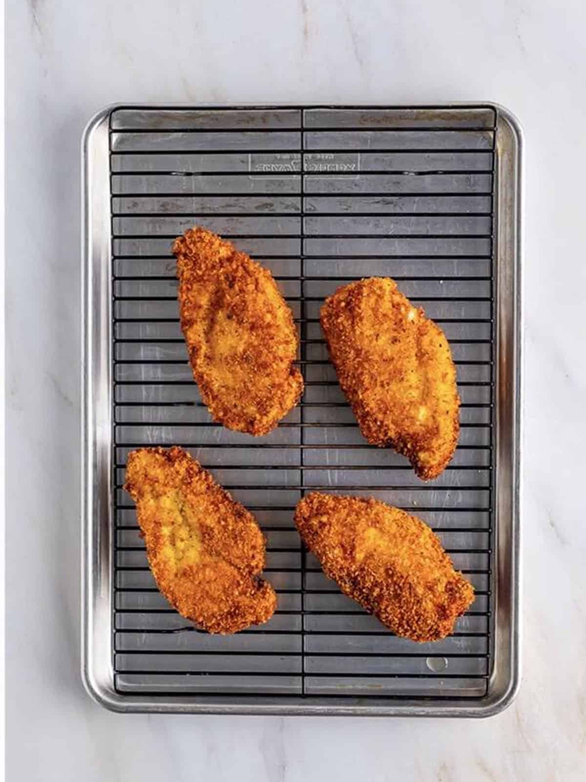 Crispy fried chicken cutlets draining on a wire rack for chicken parmesan sandwiches.