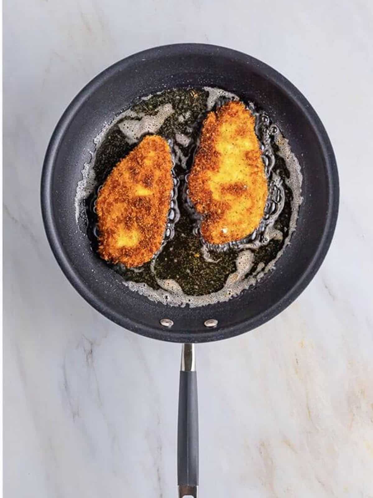 Frying breaded chicken cutlets in a skillet for chicken parmesan sandwiches.