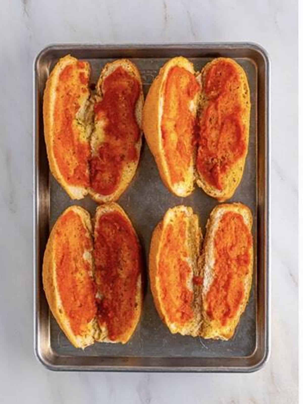 Toasted hoagie rolls spread with marinara sauce for chicken parmesan sandwiches.