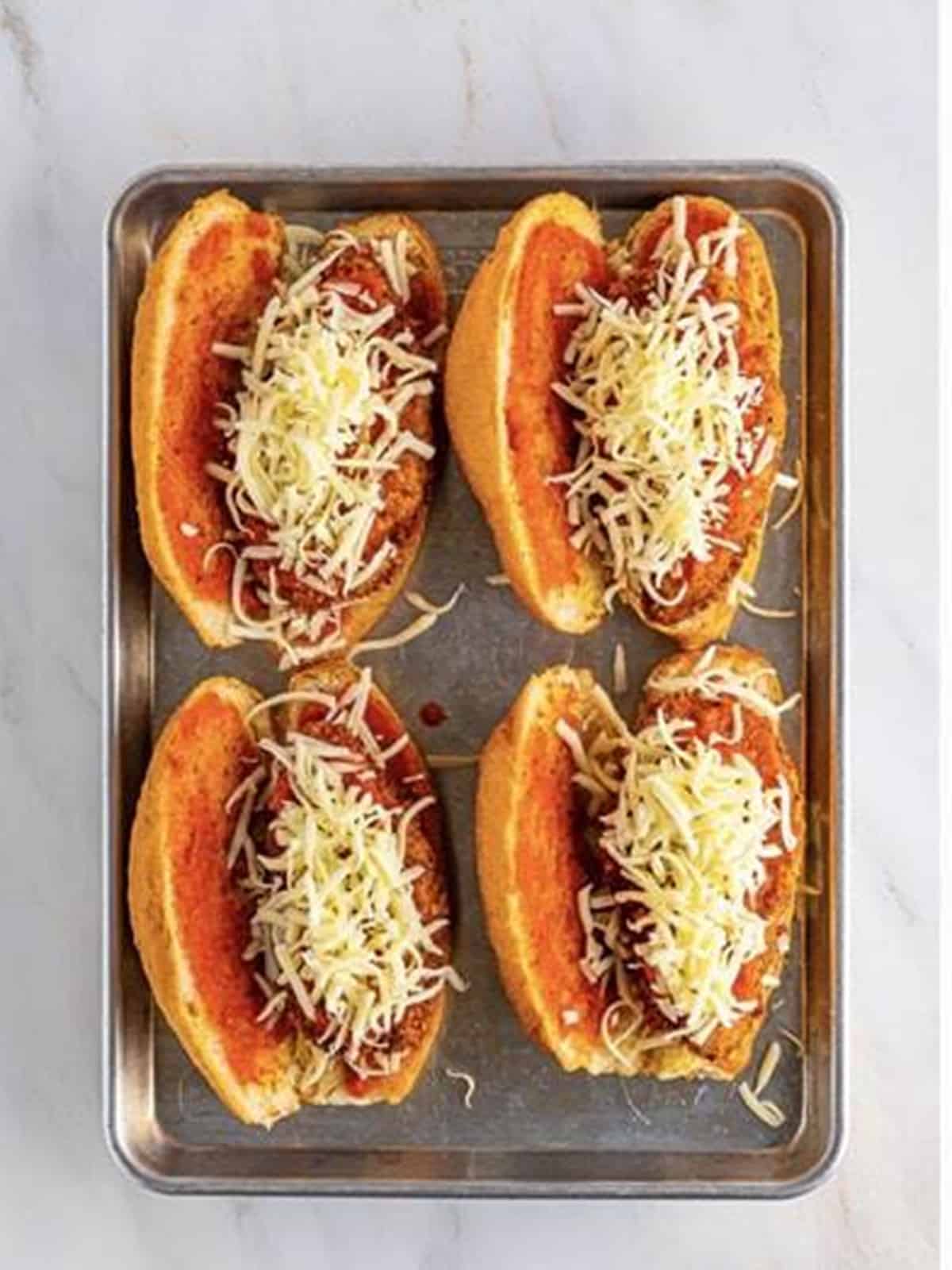 Topping the chicken parmesan sandwiches with more mozzarella cheese.