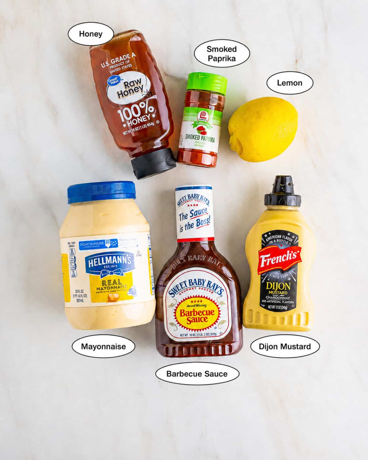Chick-Fil-A Honey Roasted BBQ Sauce Recipe ingredients laid out on a marble counter including mayonnaise, sweet bbq sauce, honey, dijon mustard, fresh lemon juice, and smoked paprika.