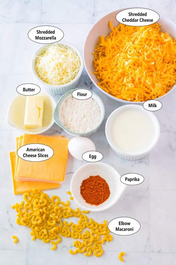 Labeled ingredients for Chick Fil A Mac and Cheese Recipe including elbow macaroni, butter, flour, milk, egg yolk, American cheese, sharp cheddar, Italian blend, salt, and paprika