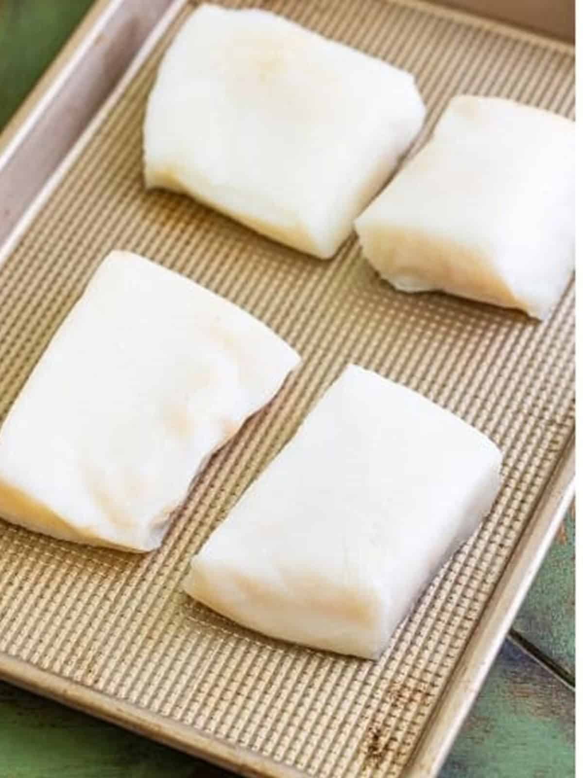 Raw Chilean sea bass filets patted dry and arranged on a sheet tray.
